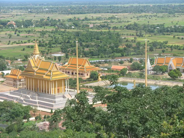 In this image we can see ancient architecture, poles, water, trees, plants, houses, and ground.